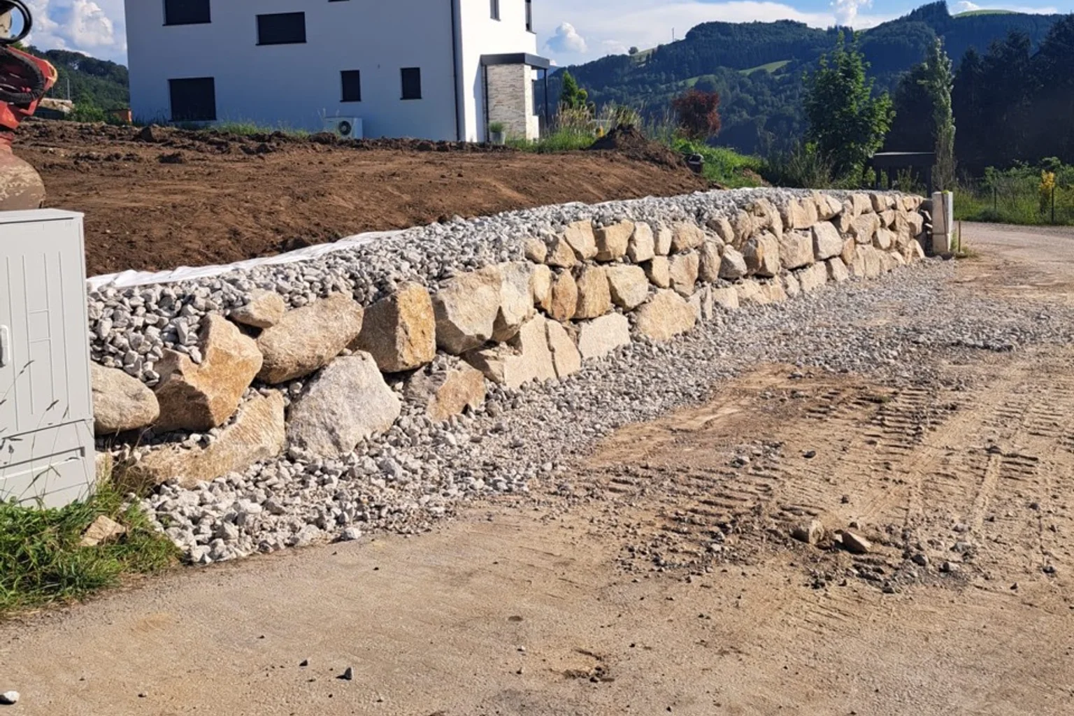 Fertiggestellte Natursteinmauer mit Schotterhinterfüllung und vorbereitetem Gelände