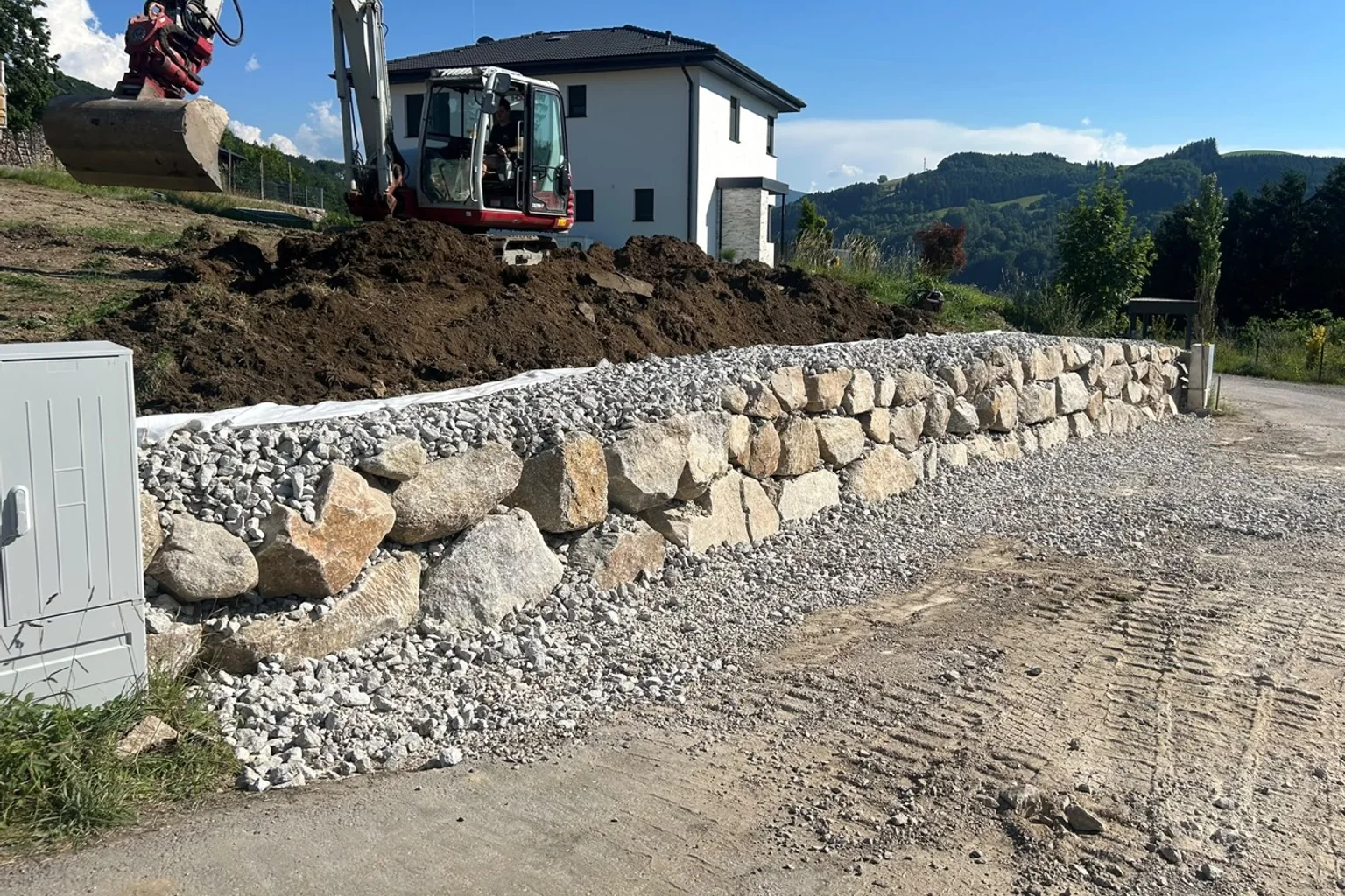 Bagger beim Aufbau einer Natursteinmauer an einem Hanggrundstück